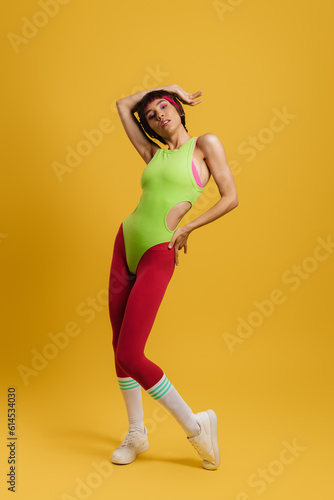 Full length of fit woman in retro styled sports clothing standing against yellow background