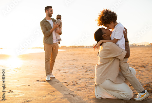 Family moments. Mother and son embracing on foreground, while father holding his little kid on hands