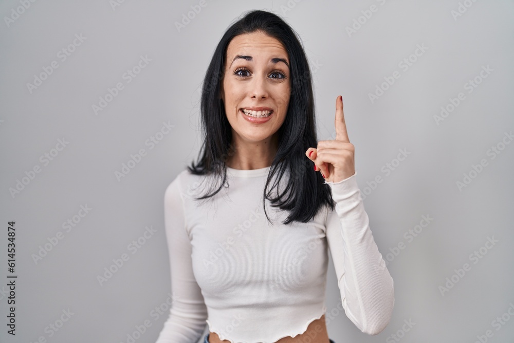 Hispanic woman standing over isolated background pointing finger up with successful idea. exited and happy. number one. Hispanic woman standing over isolated background pointing finger up with successful idea. exited and happy. number one.