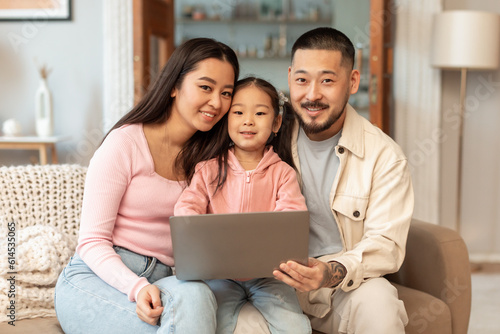 Young asian father, mother and daughter using computer at home
