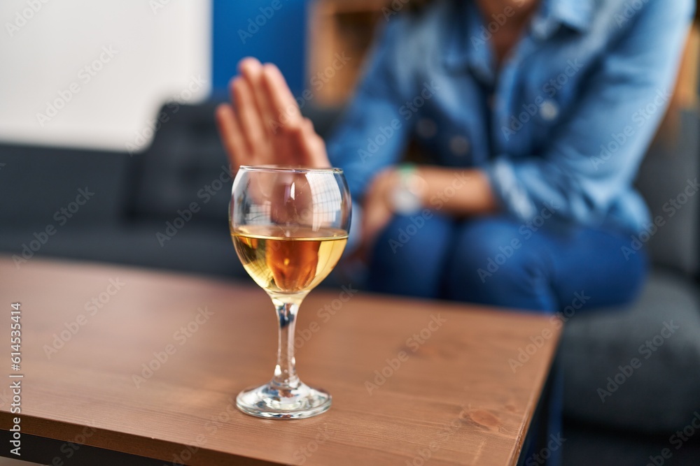 Young blonde woman rejecting glass of wine sitting on sofa at home Young blonde woman rejecting glass of wine sitting on sofa at home