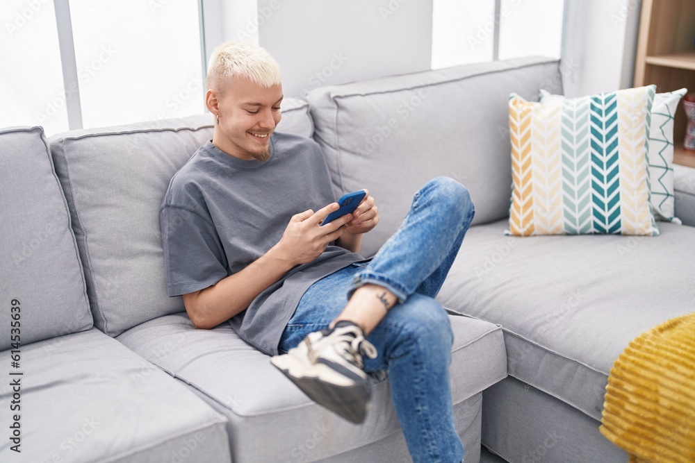 Young caucasian man using smartphone sitting on sofa at home Young caucasian man using smartphone sitting on sofa at home