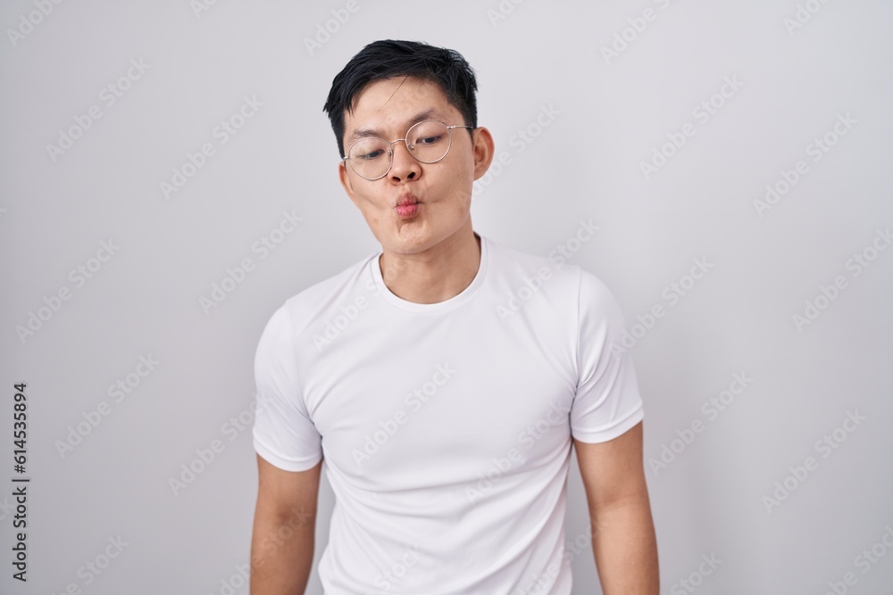 Young asian man standing over white background making fish face with lips, crazy and comical gesture. funny expression. Young asian man standing over white background making fish face with lips, crazy and comical gesture. funny expression.