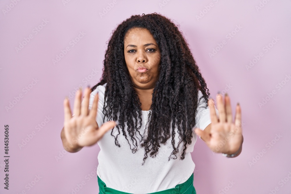 Plus size hispanic woman standing over pink background moving away hands palms showing refusal and denial with afraid and disgusting expression. stop and forbidden. Plus size hispanic woman standing over pink background moving away hands palms showing refusal and denial with afraid and disgusting expression. stop and forbidden.