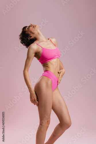 Beautiful young fit woman in underwear standing against colored background