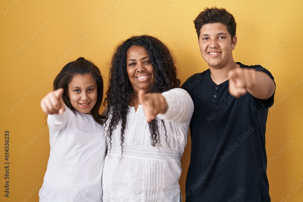 Family of mother, daughter and son standing over yellow background pointing to you and the camera with fingers, smiling positive and cheerful Family of mother, daughter and son standing over yellow background pointing to you and the camera with fingers, smiling positive and cheerful