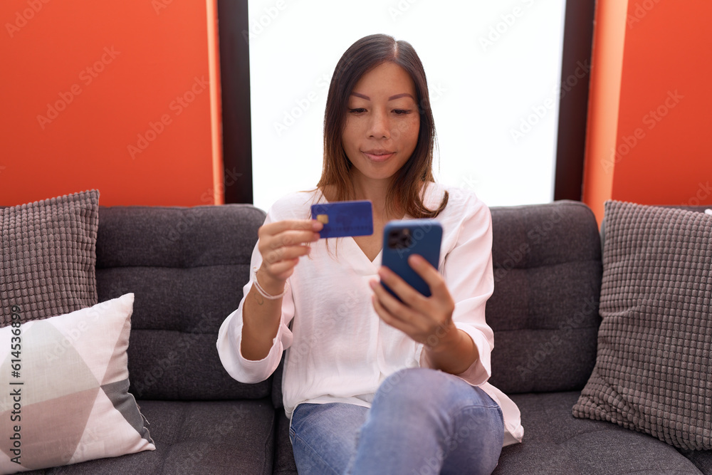 Young asian woman using smartphone and credit card sitting on sofa at home