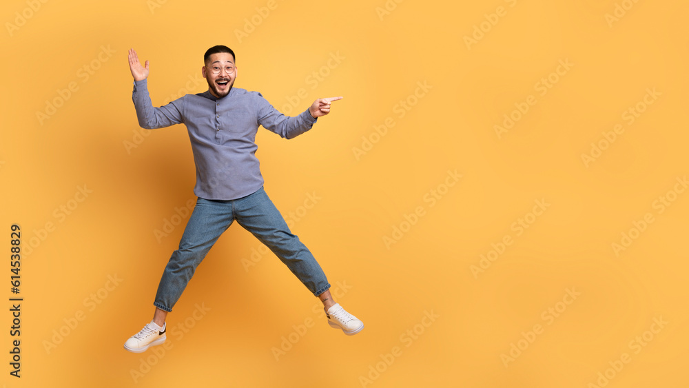 Positive Young Asian Man Showing Copy Space While Jumping In Air