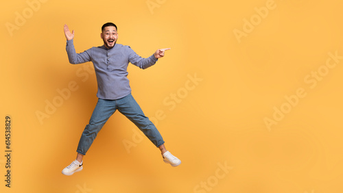Positive Young Asian Man Showing Copy Space While Jumping In Air © Prostock-studio