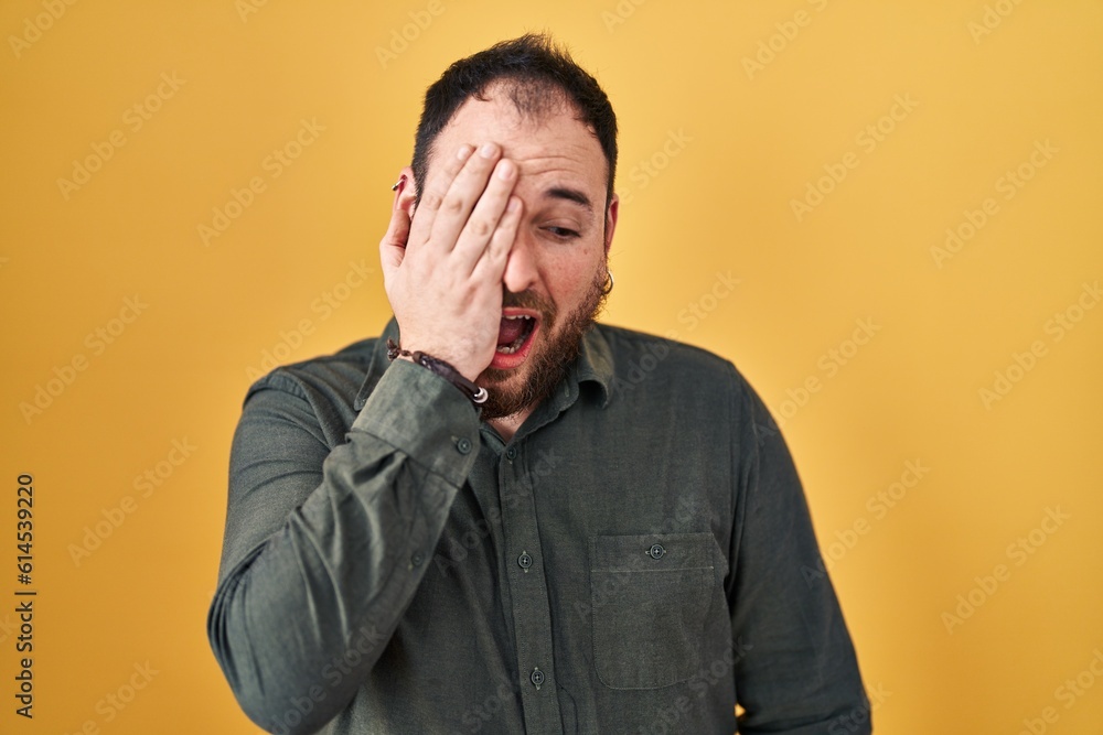 Plus size hispanic man with beard standing over yellow background yawning tired covering half face, eye and mouth with hand. face hurts in pain. Plus size hispanic man with beard standing over yellow background yawning tired covering half face, eye and mouth with hand. face hurts in pain.