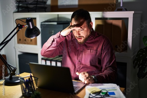 Plus size hispanic man with beard working at the office at night very happy and smiling looking far away with hand over head. searching concept.