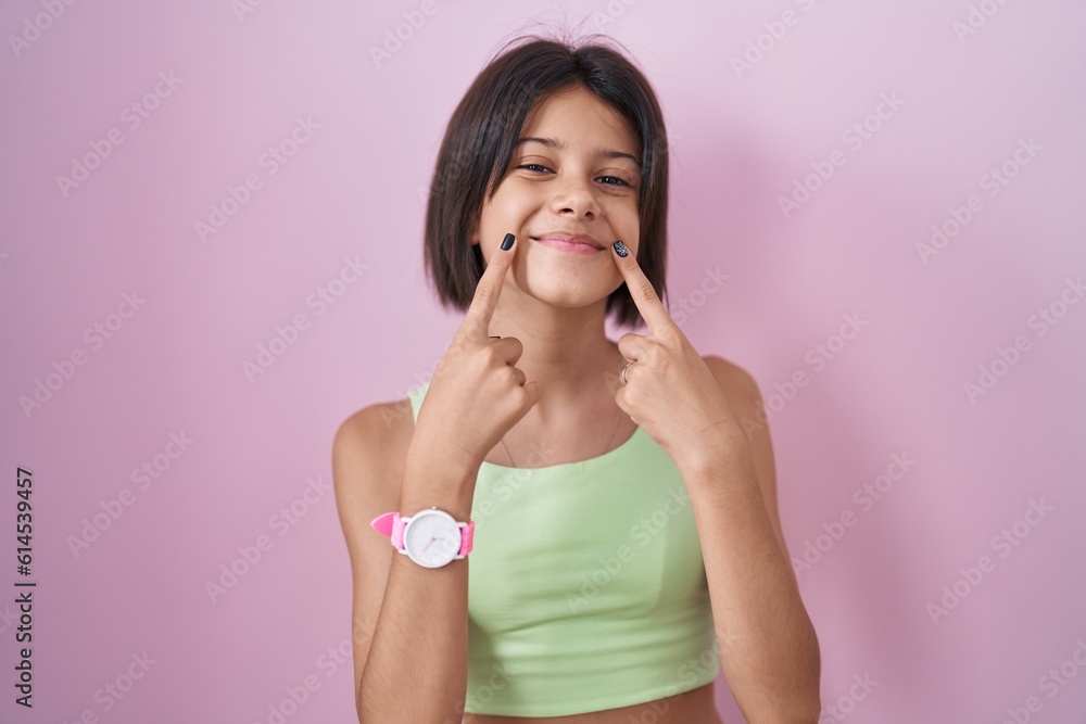 Young girl standing over pink background smiling with open mouth, fingers pointing and forcing cheerful smile Young girl standing over pink background smiling with open mouth, fingers pointing and forcing cheerful smile