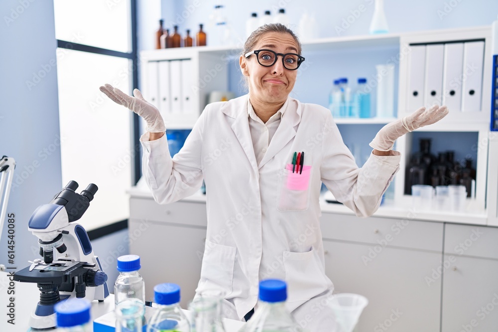 Young woman working at scientist laboratory shouting and screaming loud to side with hand on mouth. communication concept. Young woman working at scientist laboratory shouting and screaming loud to side with hand on mouth. communication concept.