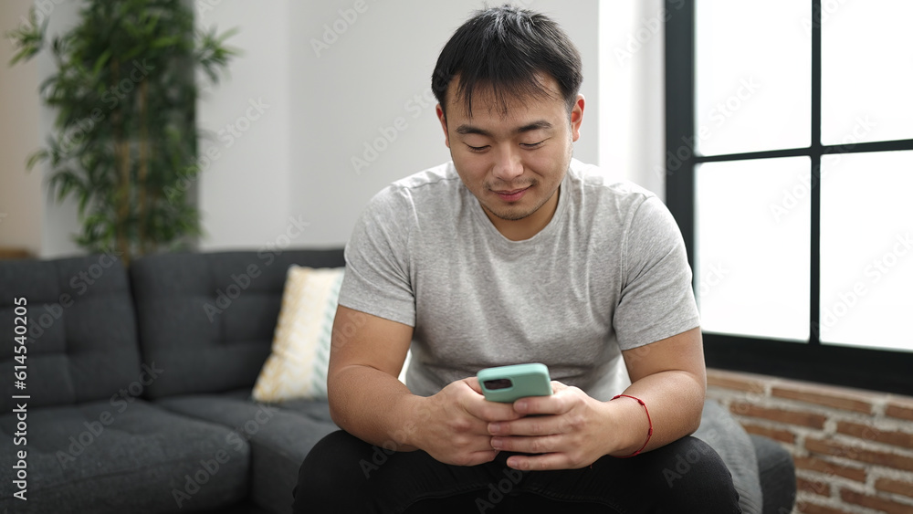 Young chinese man using smartphone sitting on sofa at home Young chinese man using smartphone sitting on sofa at home