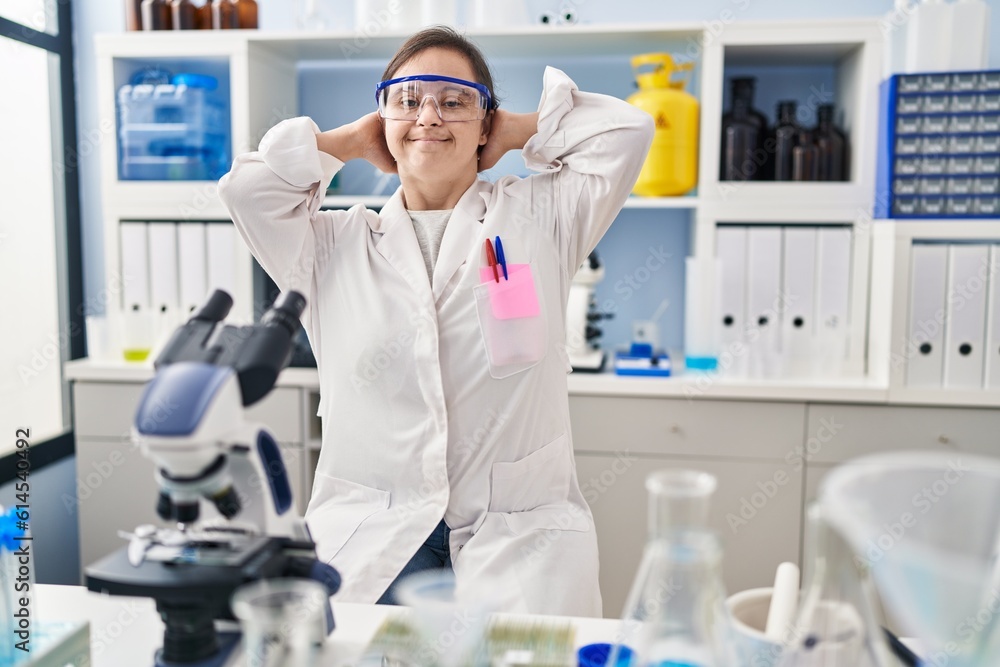 Hispanic girl with down syndrome working at scientist laboratory relaxing and stretching, arms and hands behind head and neck smiling happy Hispanic girl with down syndrome working at scientist laboratory relaxing and stretching, arms and hands behind head and neck smiling happy