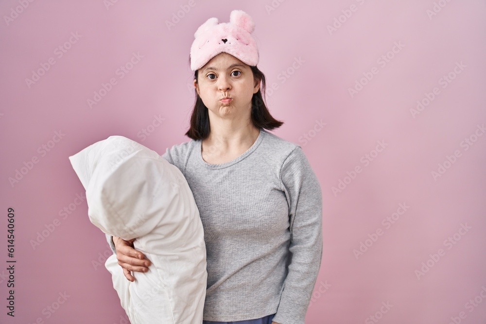Woman with down syndrome wearing sleeping mask hugging pillow puffing cheeks with funny face. mouth inflated with air, crazy expression. Woman with down syndrome wearing sleeping mask hugging pillow puffing cheeks with funny face. mouth inflated with air, crazy expression.