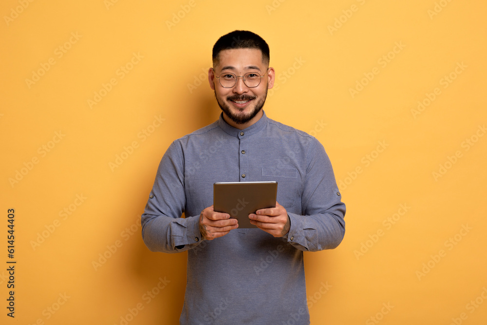 Handsome Asian Man Holding Digital Tablet In Hands And Smiling At Camera Handsome Asian Man Holding Digital Tablet In Hands And Smiling At Camera