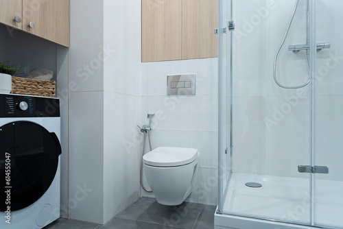 White bathroom with bath shower, toilet, wooden cabinet and washing machine. Stylish interior of washroom with wc.