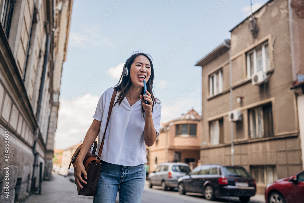 Japanese woman singing while listening music with headphones and mobile phone outside on the street