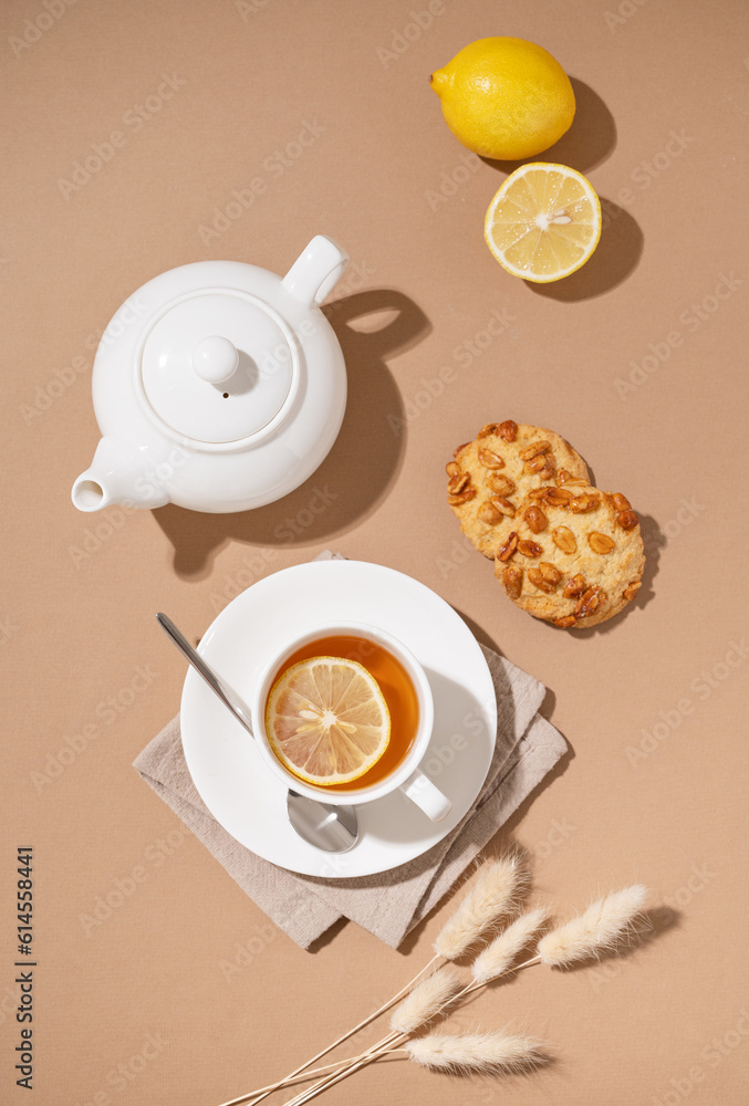 Creative layout of a cup of herbal tea with cookies, lemon and teapot on a brown background with a shadow. Healthy drink concept. Creative layout of a cup of herbal tea with cookies, lemon and teapot on a brown background with a shadow. Healthy drink concept.