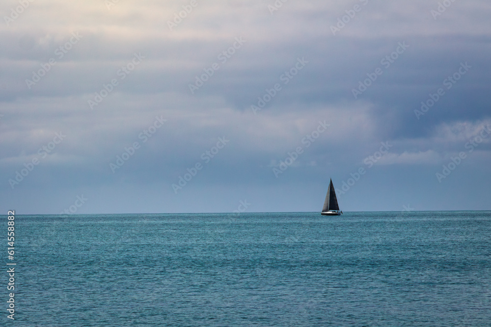 segelboot am horizont in einem blauen meer bei blauen himmel und strahlender sonne mit wolken