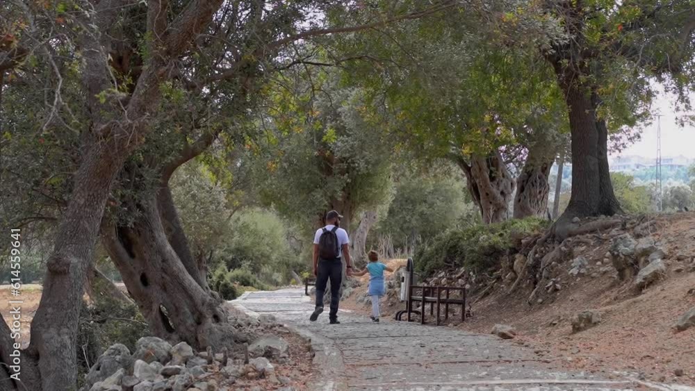 Travel with people. Caucasian father and his child boy or girl walking together path in ancient forest public park summer. Kid happily jumping. Family together leisure time activities. Travel with people. Caucasian father and his child boy or girl walking together path in ancient forest public park summer. Kid happily jumping. Family together leisure time activities.