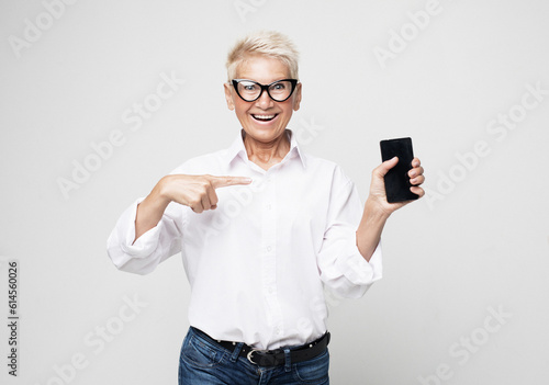 Attractive elderly female with pixie blonde hair presents new smartphone over light grey