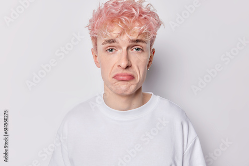 Portrait of displeased pink haired man has sad upset or bored expression purses lips feels discontent melancholic face reflects his current state of emotion dressed casually isolated over white wall