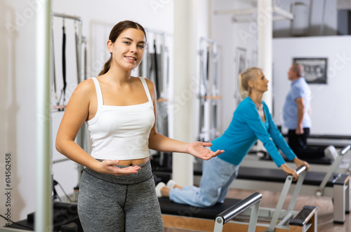 Portrait of young European woman in sportswear smiling at camera against group class in Pilates fitness studio