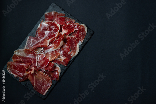 Tradition in every slice: the exquisiteness of acorn-fed Iberian ham on a black background.
