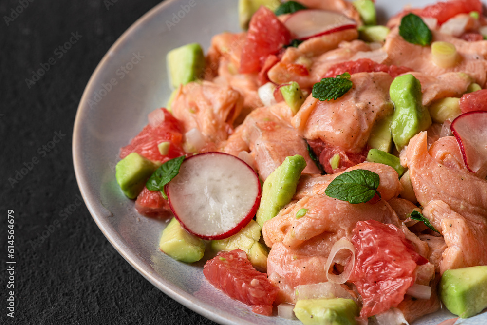 Chilean salmon seviche with grapefruit, avocado, radish, onion and mint in a plate with fork on black background. close up Chilean salmon seviche with grapefruit, avocado, radish, onion and mint in a plate with fork on black background. close up