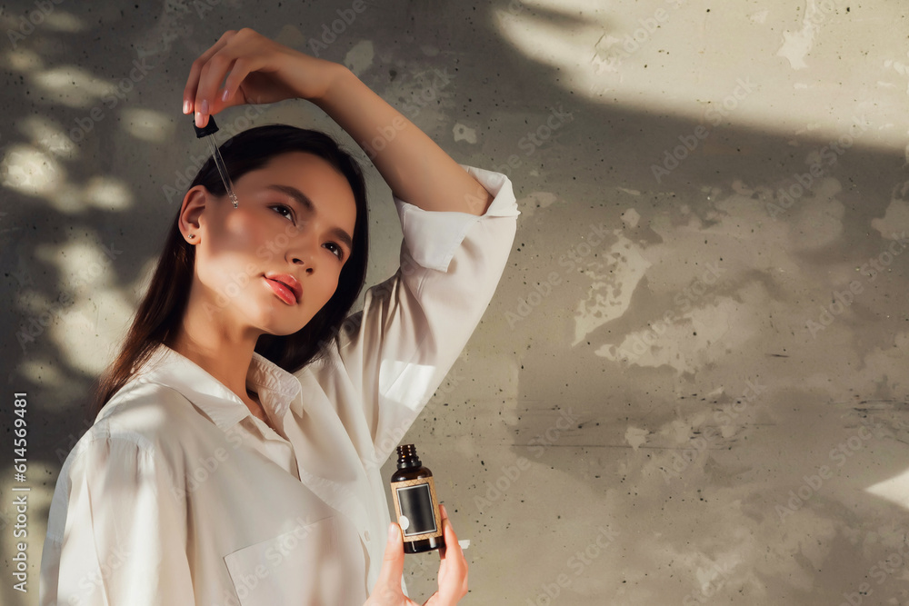 Lovely young lady dripping massage oil drops with pipette to face skin