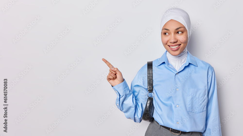Young religious Muslim woman dressed elegantly in formal attire confidently points towards empty space on white background suggests to discover new possibilities isolated over white background Young religious Muslim woman dressed elegantly in formal attire confidently points towards empty space on white background suggests to discover new possibilities isolated over white background