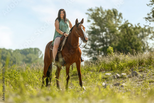 A young woman riding her bay brown horse in front of a rural summer landscape  female equestrian in summertime © Annabell Gsödl