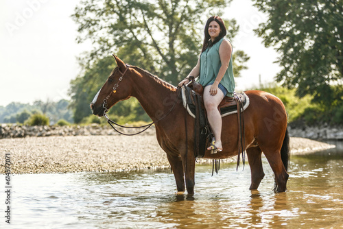 Equestrian and horse cooling down at a hot summer day  A young woman and her bay brown andalusian x arab horse gelding having fun in the water of a river outdoors