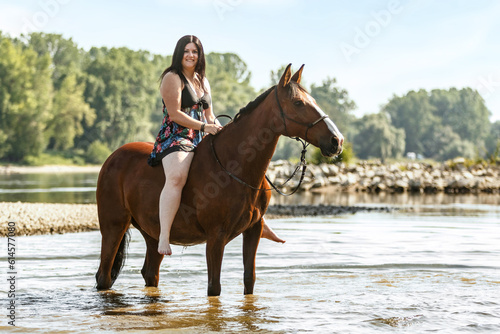 Equestrian and horse cooling down at a hot summer day: A young woman and her bay brown andalusian x arab horse gelding having fun in the water of a river outdoors © Annabell Gsödl
