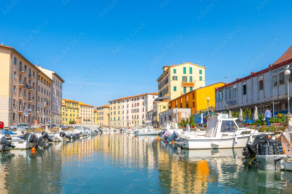 Colorful residential buildings reflect off the water in the boat filled canals at the old port of Livorno, Italy, in the Tuscany region.