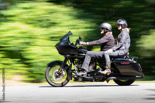 Panning photo of a man and woman dressed in black clothing on a black motorcycle.