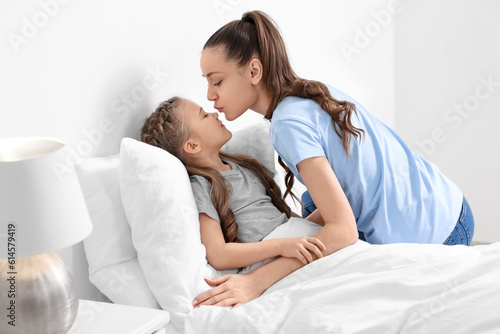 Happy mother kissing her cute daughter on bed at home