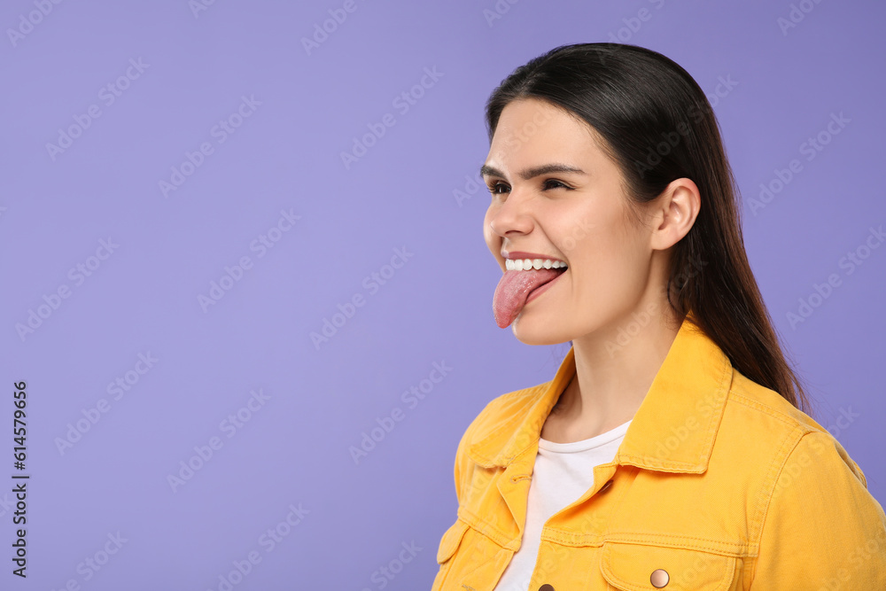 Happy young woman showing her tongue on purple background. Space for text Happy young woman showing her tongue on purple background. Space for text