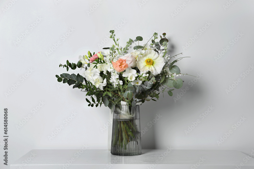 Bouquet of beautiful flowers in vase on table against white wall Bouquet of beautiful flowers in vase on table against white wall