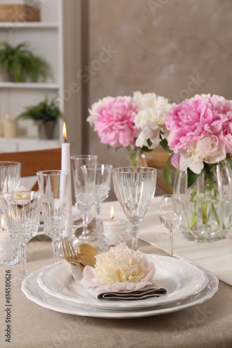 Stylish table setting with beautiful peonies and burning candles indoors