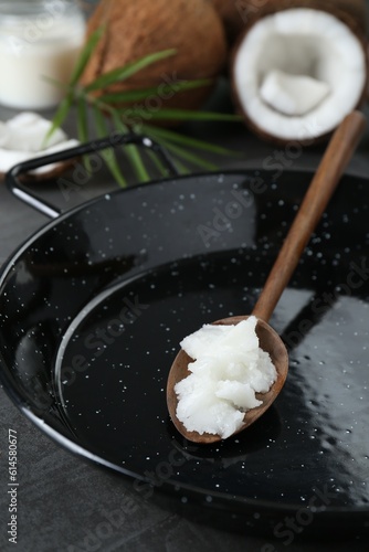 Frying pan with organic coconut cooking oil and wooden spoon on grey table