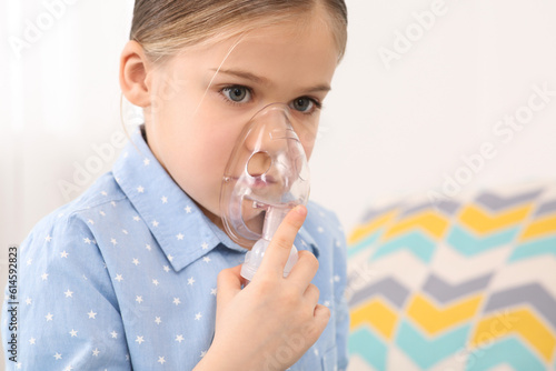 Sick little girl using nebulizer for inhalation indoors