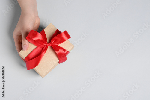 Fototapeta Naklejka Na Ścianę i Meble -  Woman holding gift box with red bow on white background, above view. Space for text