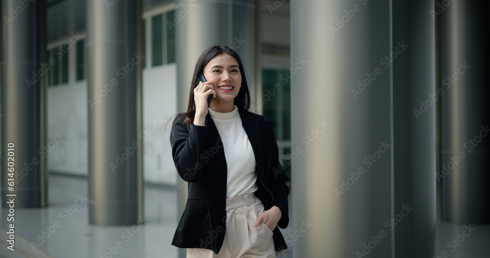Young Asian businesswoman in suit talking on  smartphone while walking
