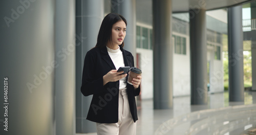 Young Asian business woman in suit holding mobile phone with takeaway coffee Free Download Young Asian business woman in suit holding mobile phone with takeaway coffee - GFXLoad