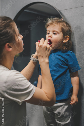 Shot of caucasian mother teaching her daughter to brush her teeth in the bathroom. Personal oral hygiene and dental care concept.