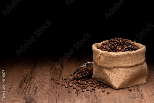 The many coffee beans and bag and scoop are placed around on a wooden table in a warm, light atmosphere, on dark background, with copy space.