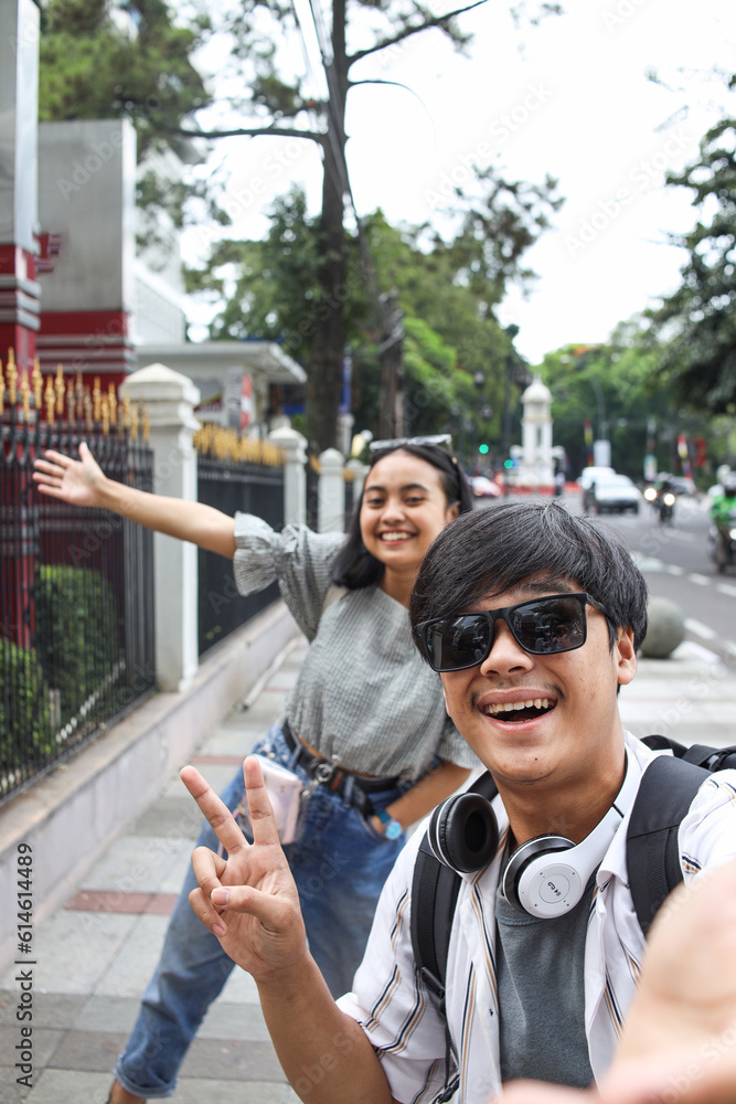 POV of young Asian man in sunglasses and happy joyful woman smiles and taking selfie together by mobile phone on street